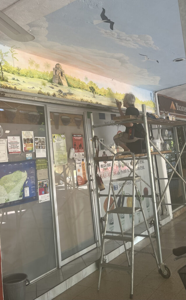 a person painting a mural by hand over a shop doorway